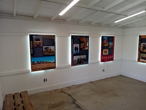 A small white room with several illuminated informational posters on the walls and a wooden bench on the floor.