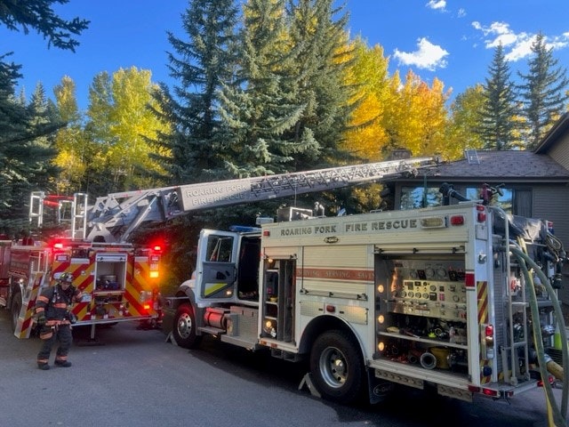 Fire trucks with extended ladder, firefighter, and trees.