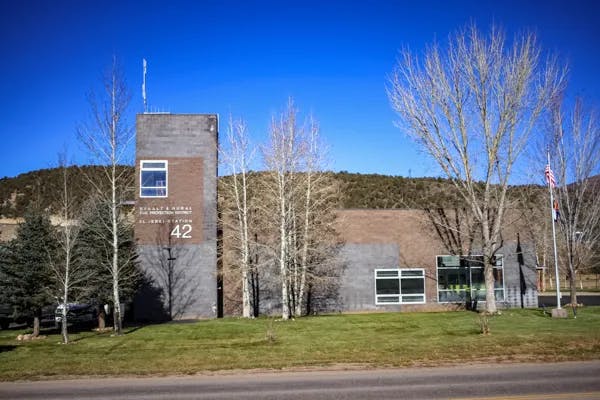A modern building with the number 42, bare trees, and grass in front of a hill under a clear sky.