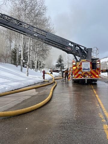 Firefighters and a fire truck with an extended ladder on a snowy road.