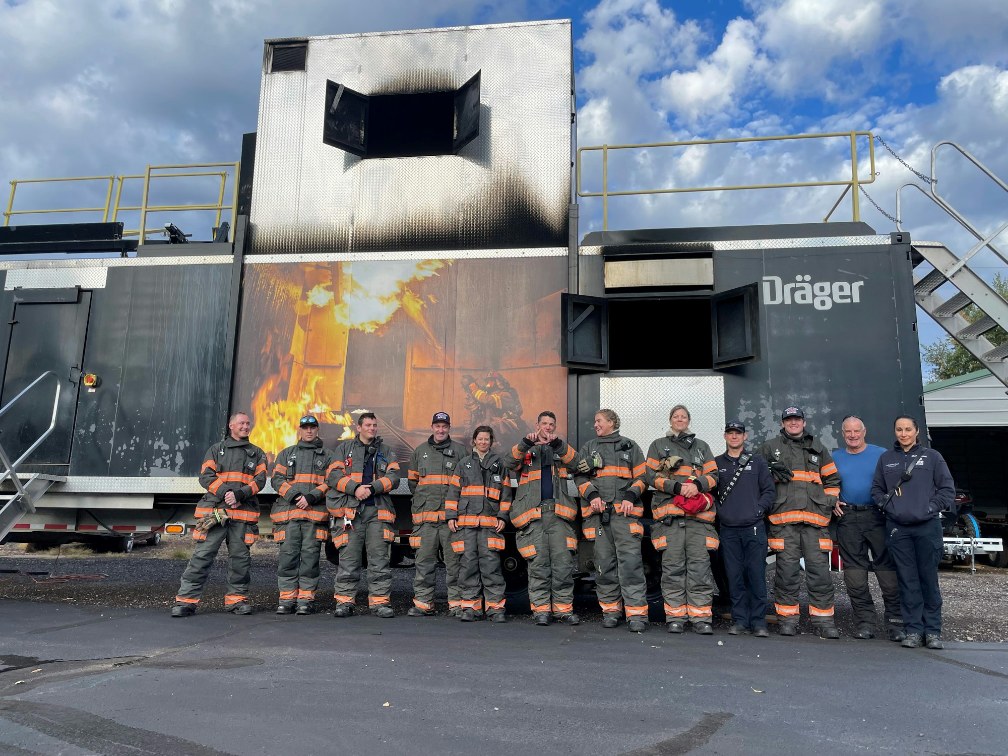 Firefighters in gear posing in front of a training facility with simulated flames.
