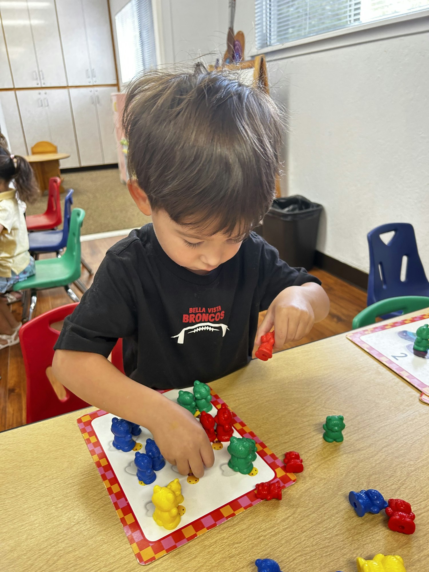 A child in a classroom is sorting colorful bear counters on a table.