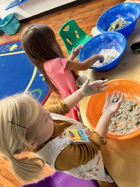 Two children playing with sensory bins filled with flour and other materials.