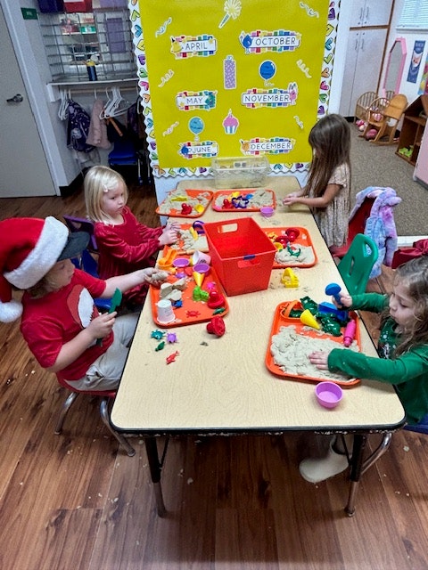Children playing with colorful playdough and toys at a table in a classroom setting.