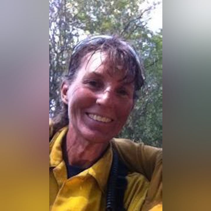 A smiling person in a yellow jacket with wet hair, possibly after rain or exercise.