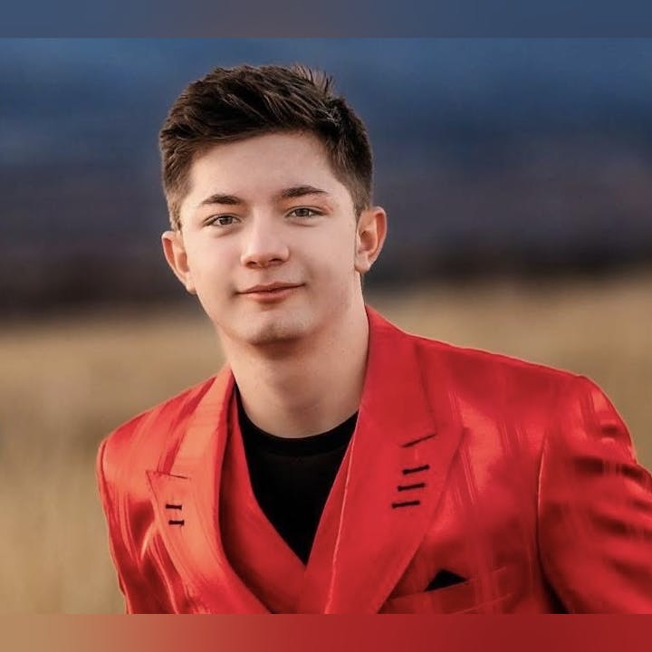 A person in a red suit stands outdoors with a blurred background.
