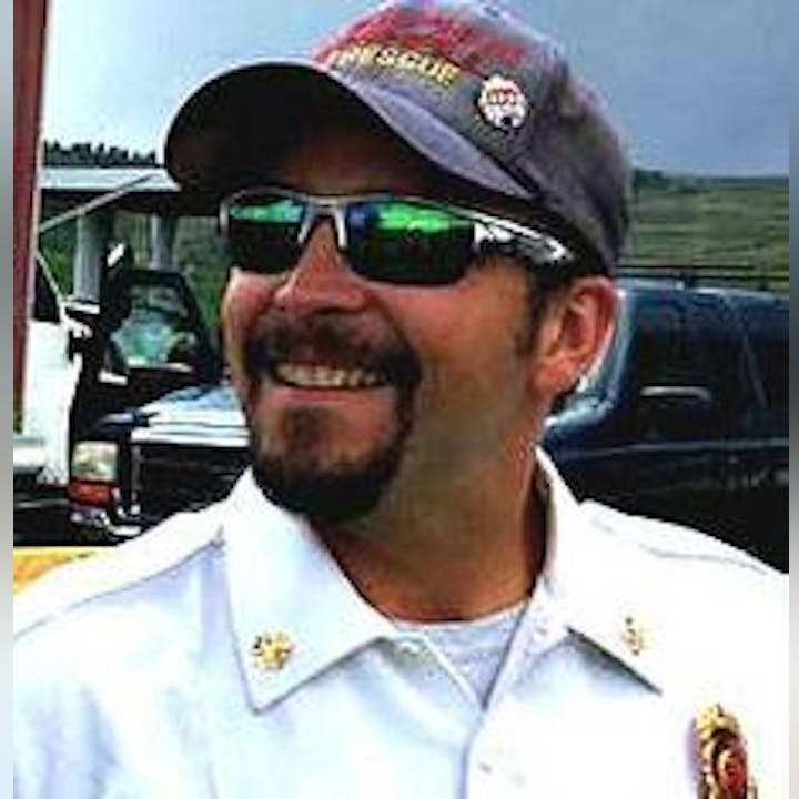 A smiling man wearing sunglasses and a rescue/firefighter uniform cap.