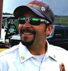 A smiling man wearing sunglasses and a rescue/firefighter uniform cap.