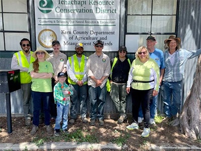Group of people posing in front of a sign that reads "Tehachapi Resource Conservation District, Kern County Department of Agriculture and Measurement Standards".