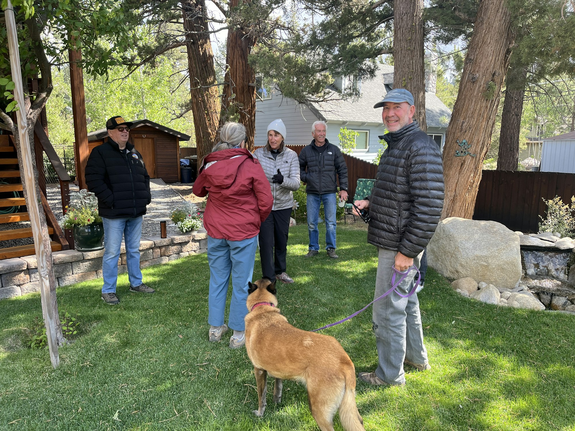 A group of people chatting outdoors in a garden with a dog.
