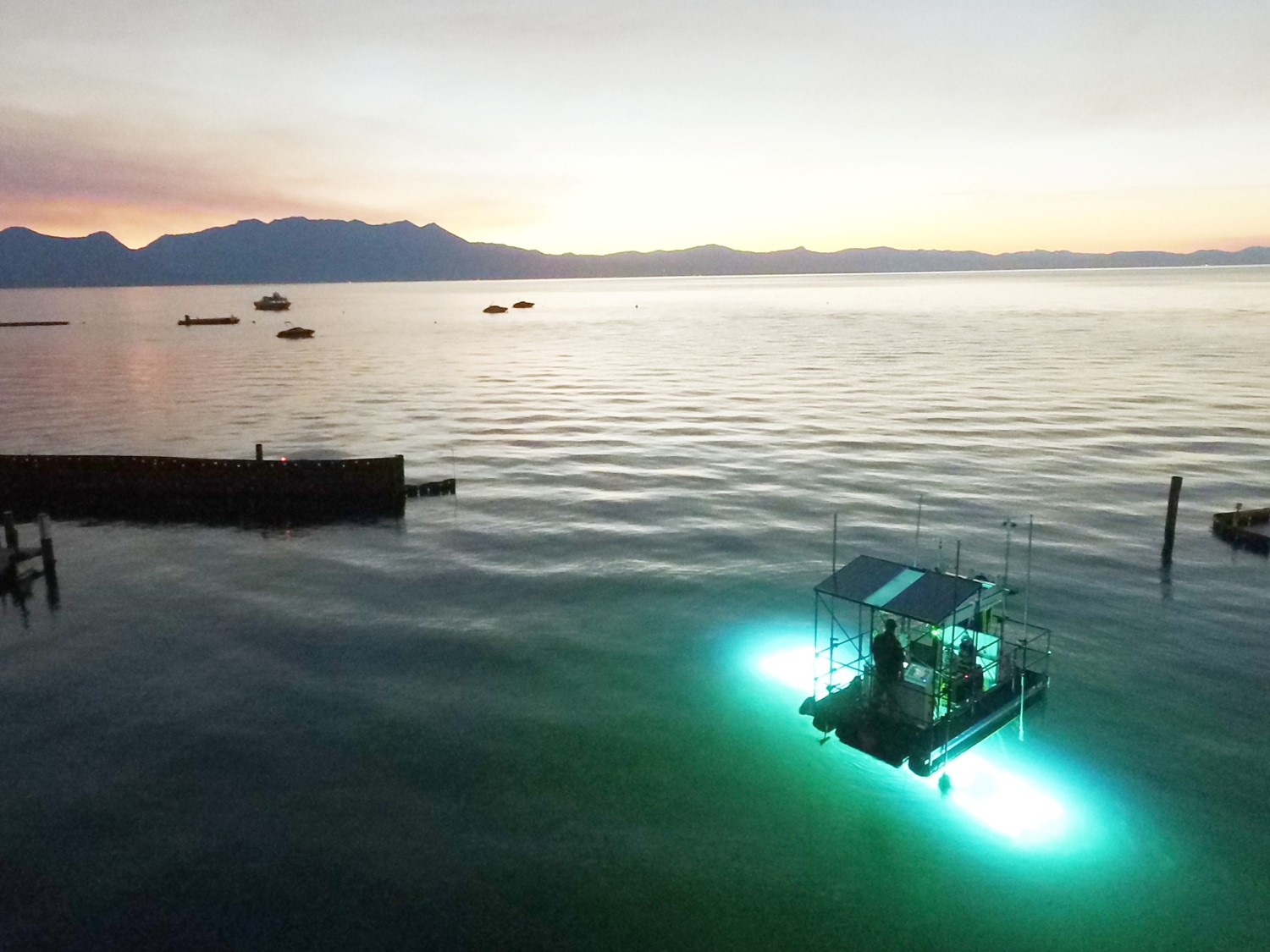 A serene seascape at dusk with illuminated platform on the water and mountains in the distance.