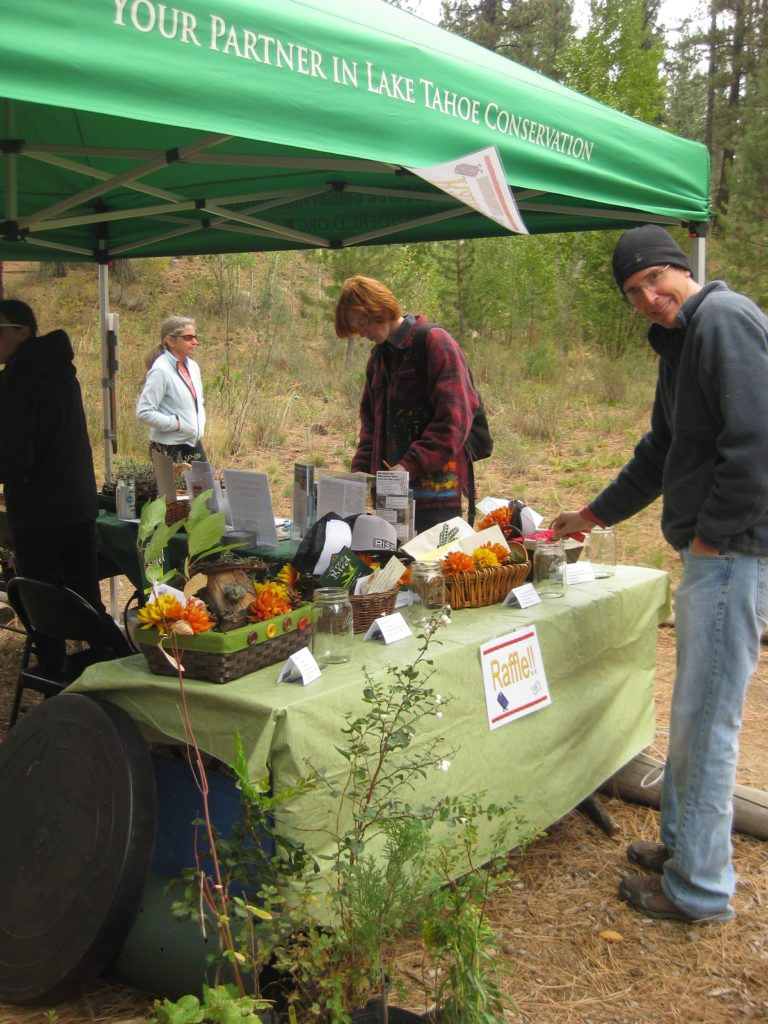An outdoor conservation event with a raffle booth, people, and promotional materials under a tent.