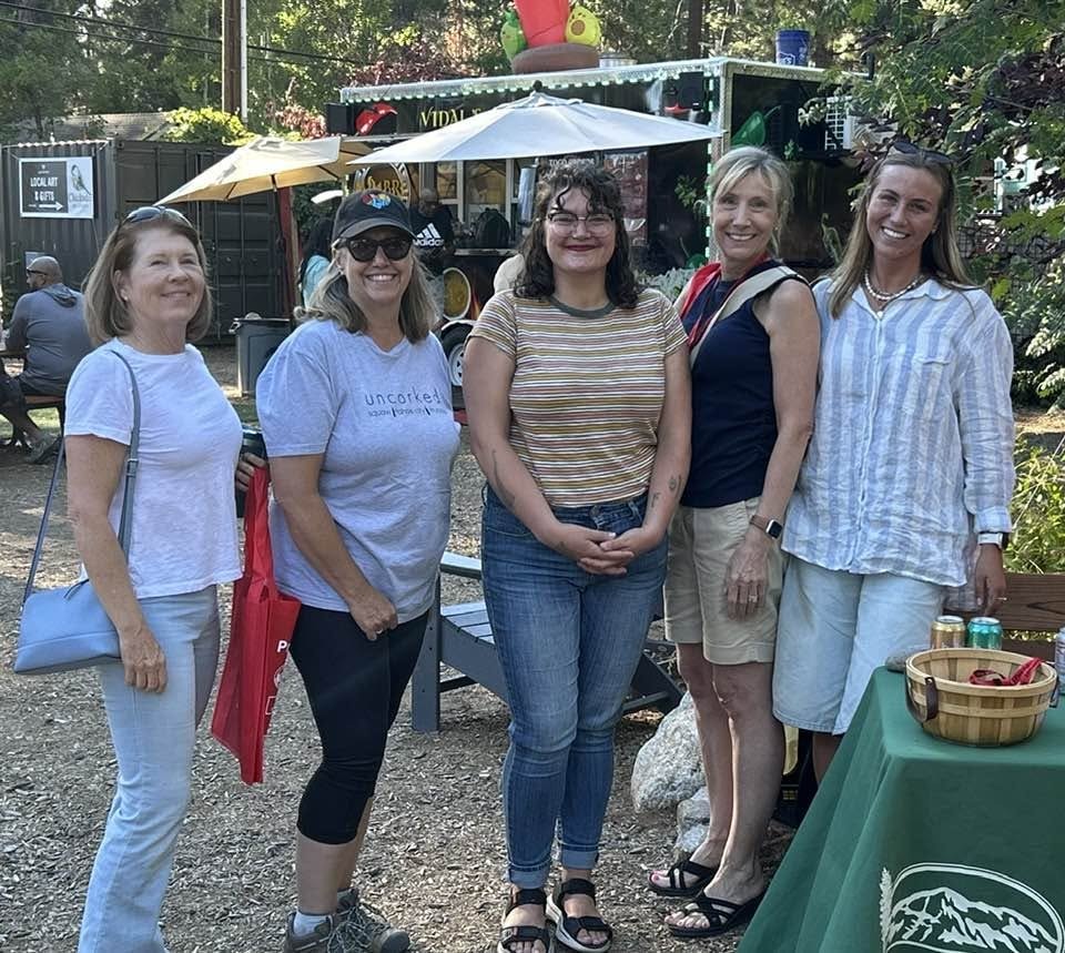 A group of five women pose together outdoors, smiling in front of food trucks and vibrant scenery.