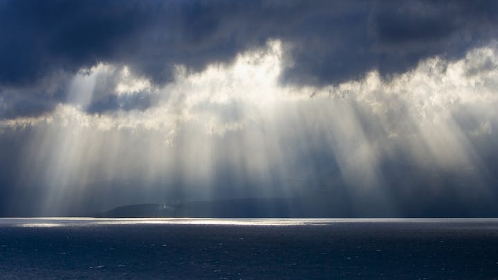 Sunbeams breaking through clouds over a serene sea.