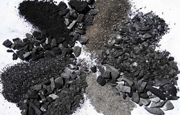 Piles of different types of charcoal arranged in a circle on a white surface.