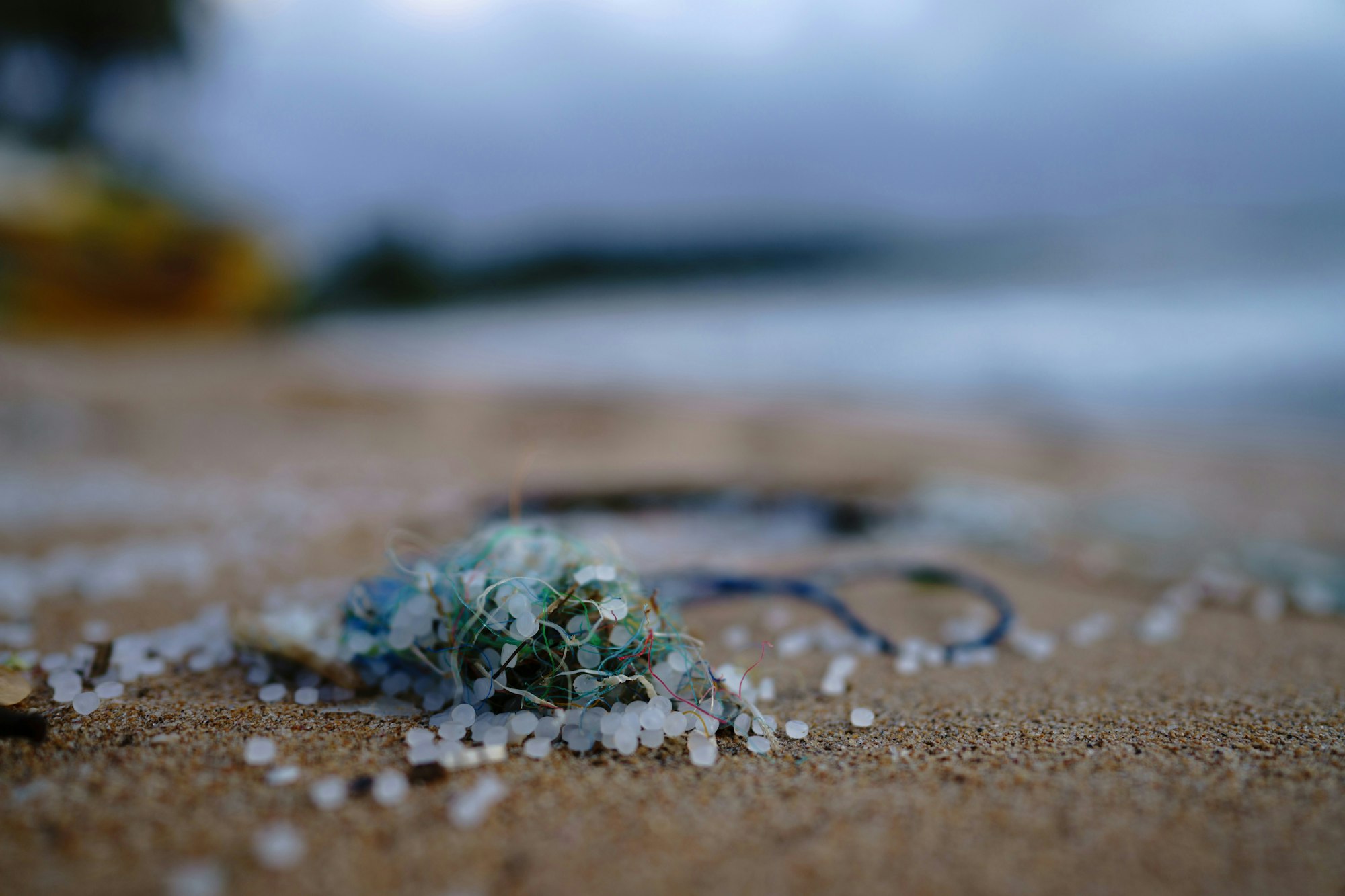 Beach sand with scattered plastic pellets and tangled debris.