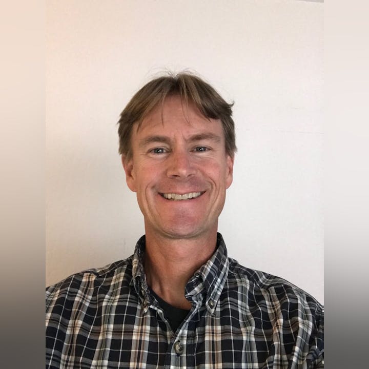 A smiling person in a plaid shirt against a plain background.