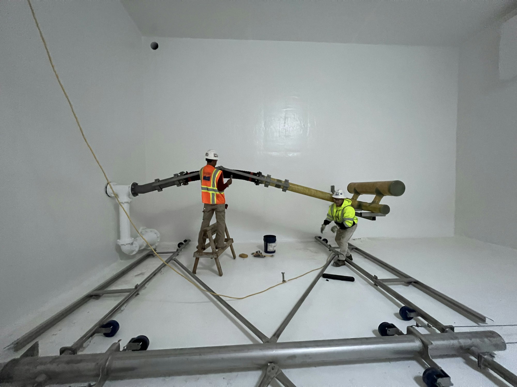 Two workers in safety gear install metal pipes in the completed, white backwash reclaim tank.