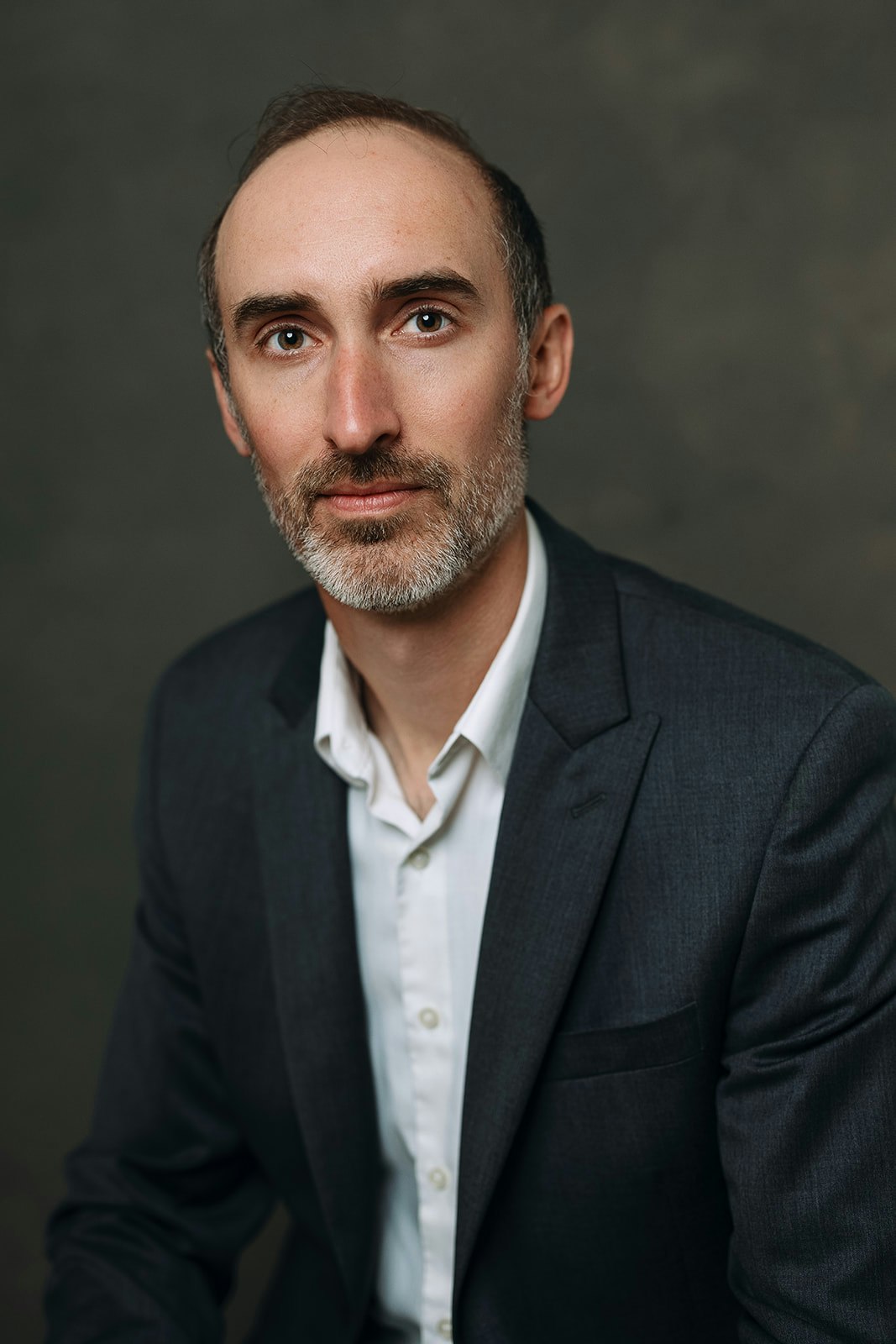 Headshot of Eric Harris, who has dark hear and is in front of a dark background in a black suit and white button-down white shirt.