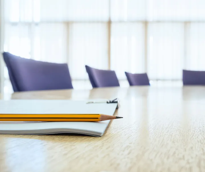 Pencil and notebook on a conference table, with blurred chairs in the background.