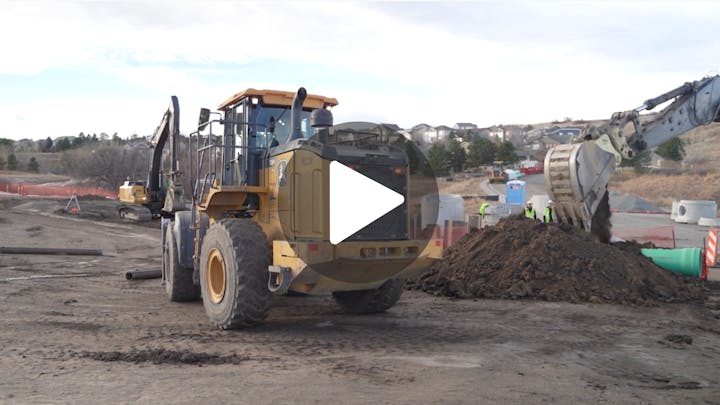 A construction site featuring heavy machinery, including a loader and excavator, moving dirt with workers in the background.