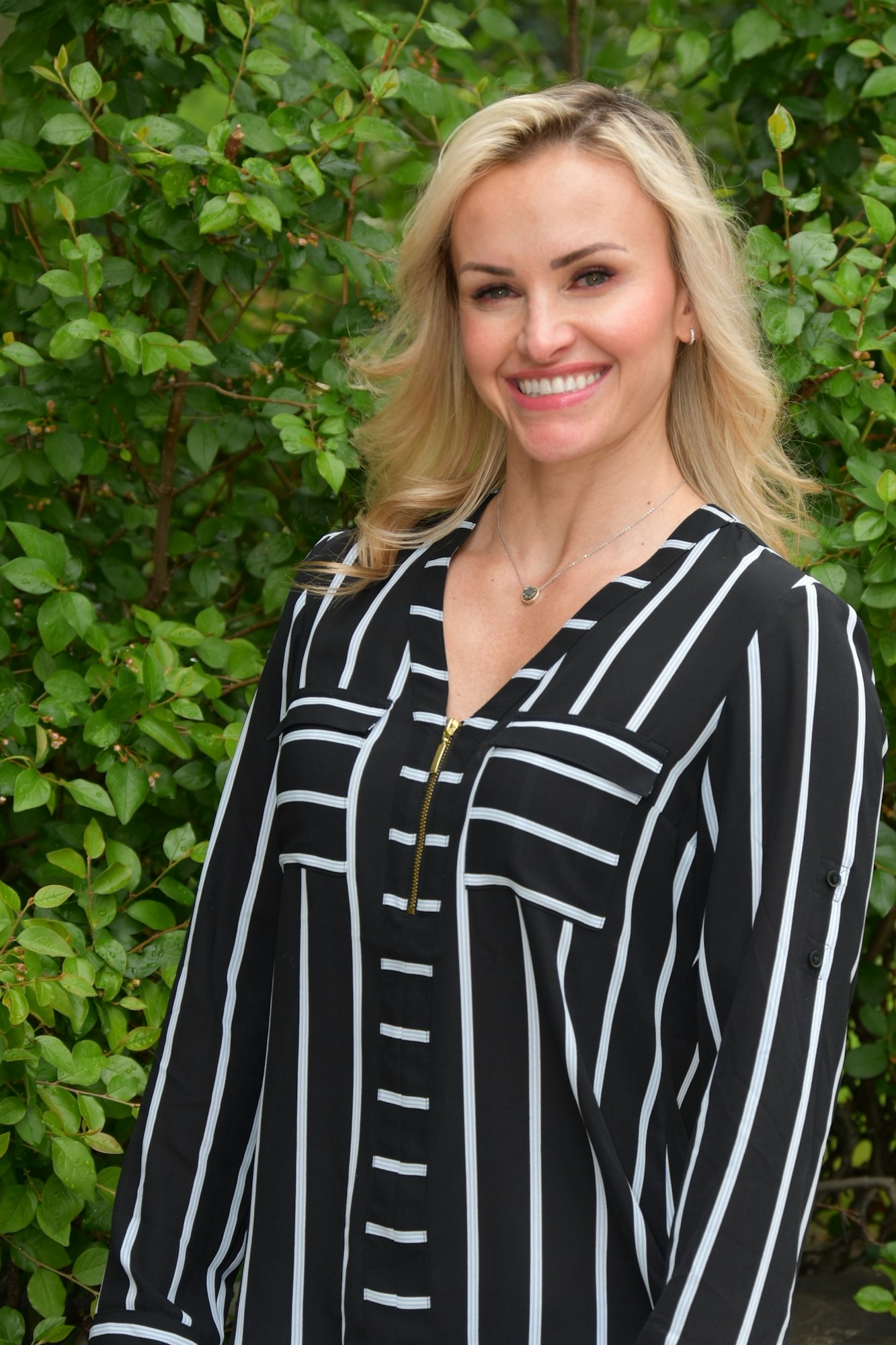 Headshot of Allison in a white and black striped dress against a leafy background.