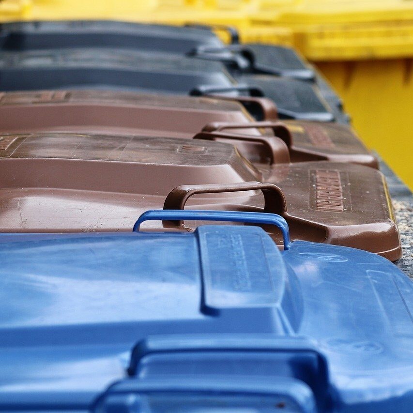 Various colored trash bins lined up, featuring blue, brown, and yellow lids.