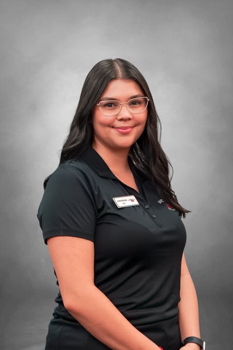 The image features a woman in a black polo shirt, smiling, with long dark hair and glasses, set against a gray background.