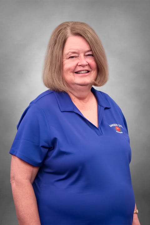 A smiling woman with shoulder-length hair, wearing a blue polo shirt with "Garden City" logo, set against a gray background.
