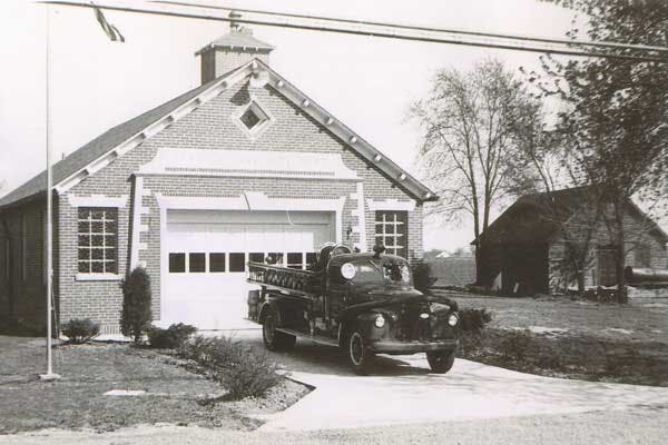 A vintage fire truck parked outside a small brick fire station.
