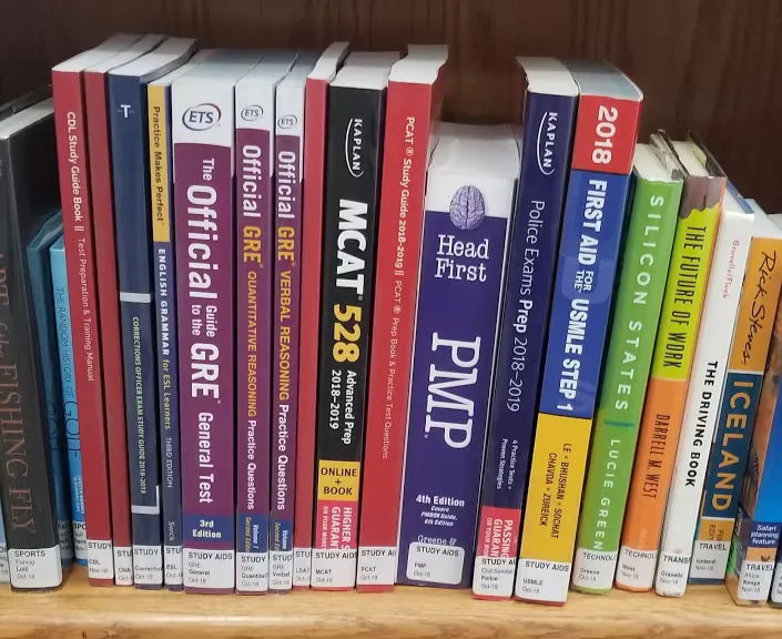 A bookshelf filled with various study guides and preparation books for exams like GRE, MCAT, and PMP.