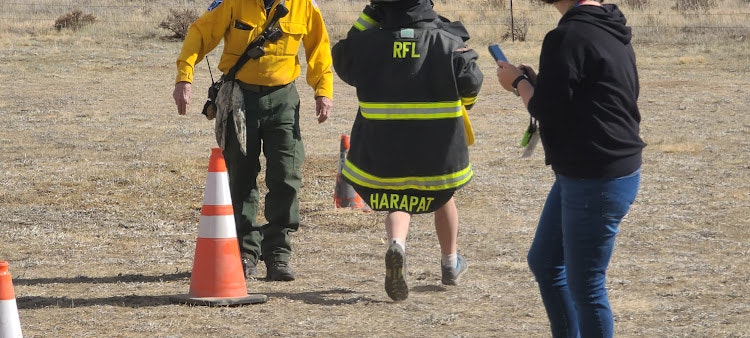 Three people walking outside, one in firefighter gear, others in casual clothes, with a traffic cone visible.