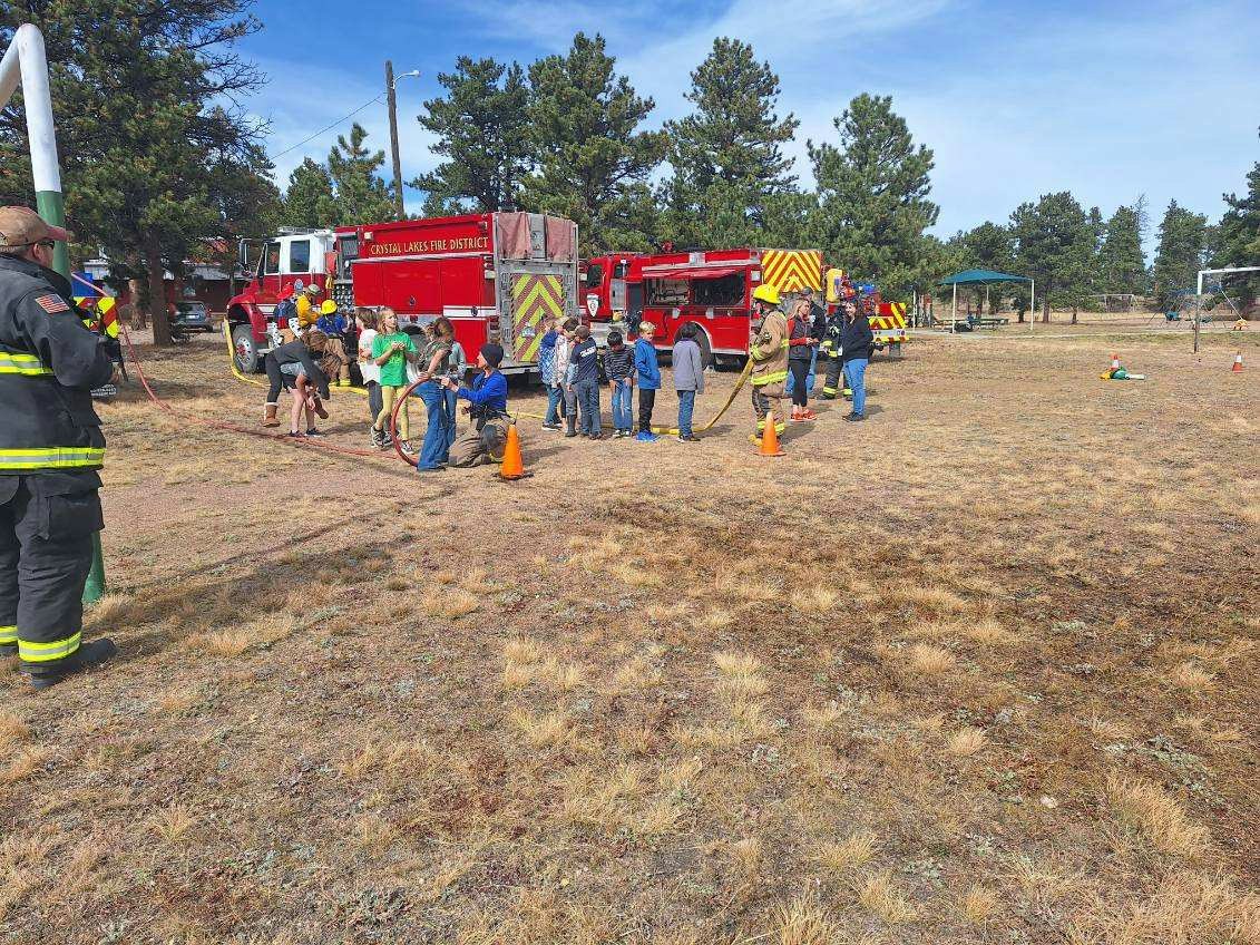 Children interact with firefighters and fire trucks in a grassy area during a community event.