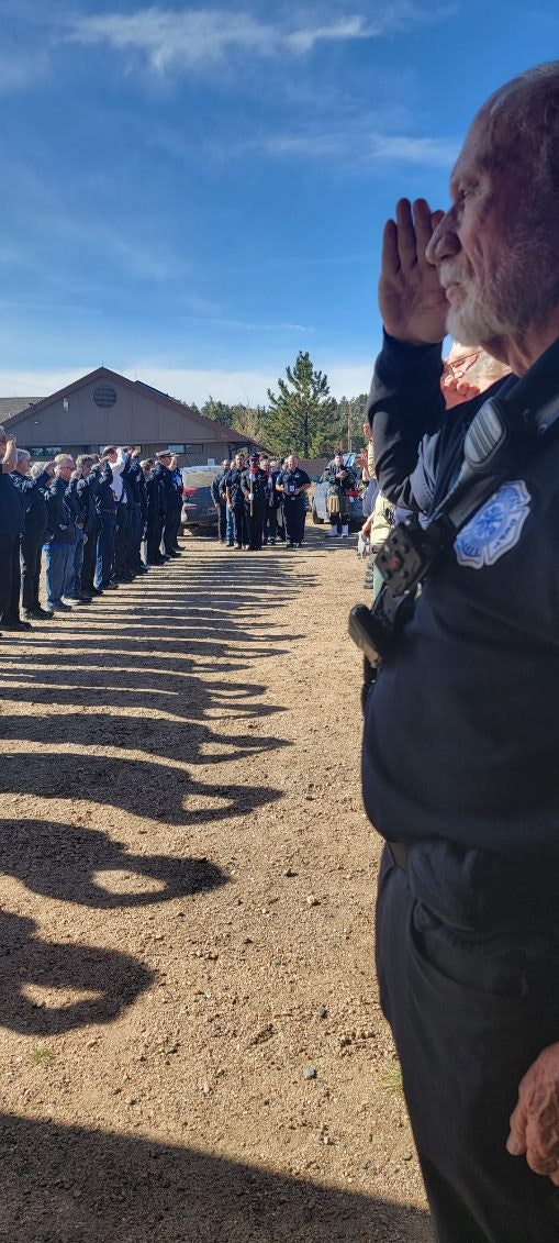 A person saluting, many people in uniforms lined up, possibly a formal event. Shadows on the ground, sunny day.