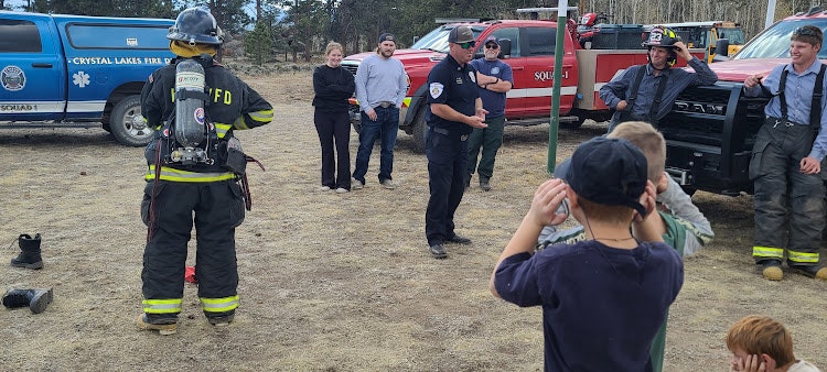 A firefighter, an ambulance, people, and a child taking a picture.
