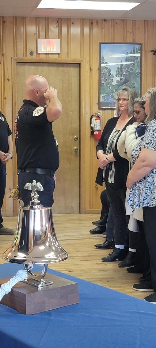A uniformed person saluting, attendees looking on, and a large trophy on a blue-draped table.