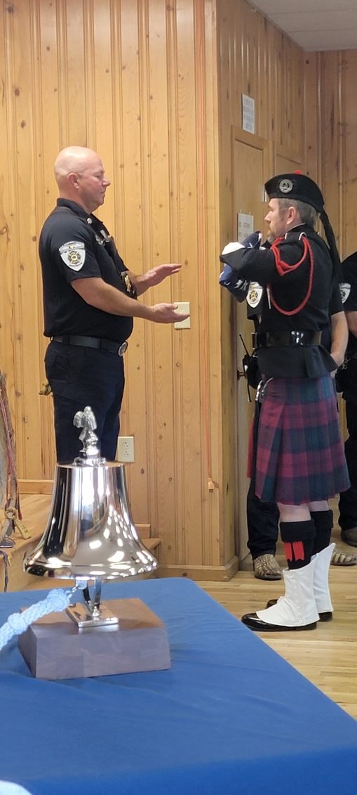 A police officer conversing with a person in a traditional kilt outfit, indoors, beside a bell on a table.