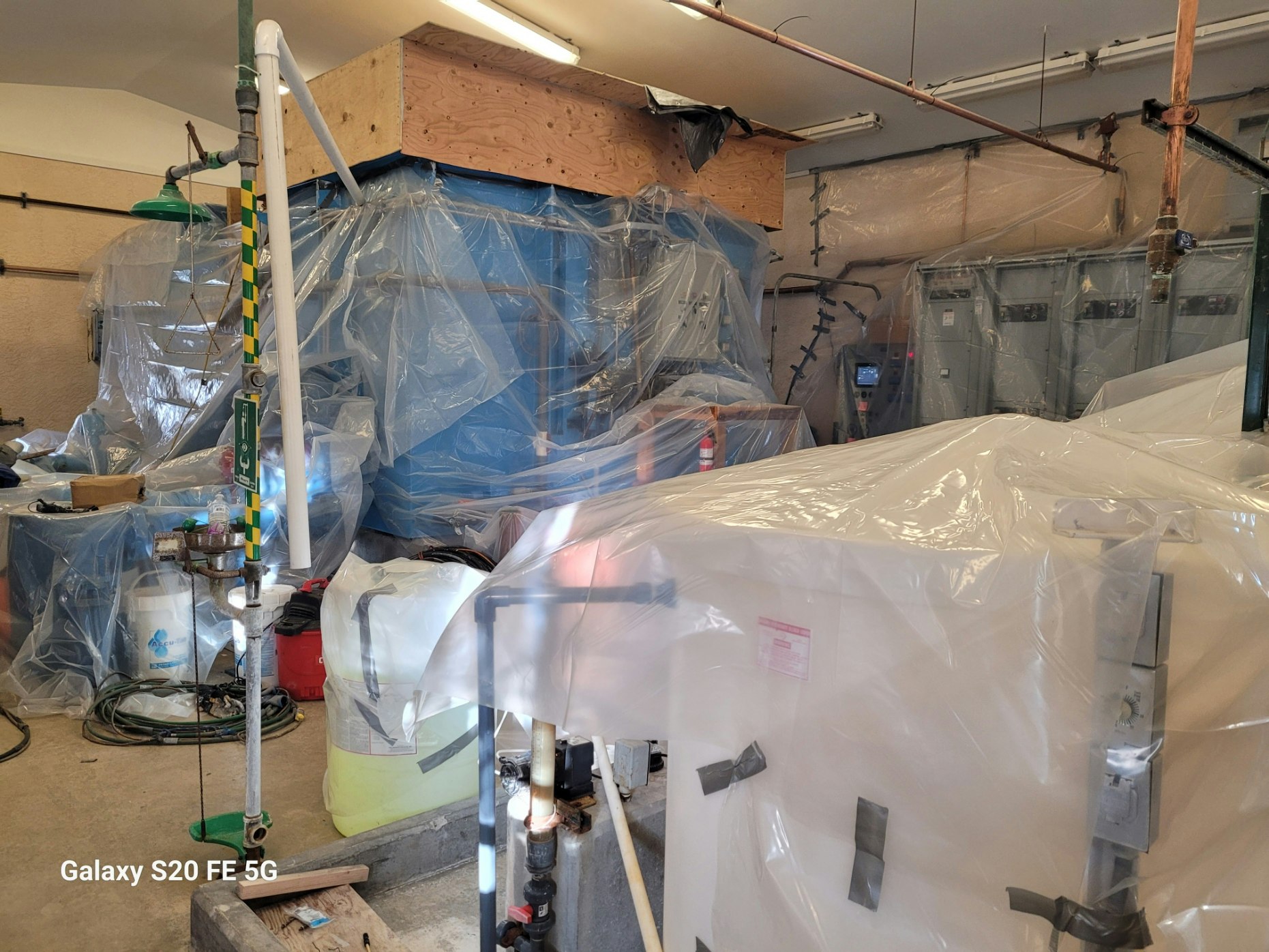 A workshop with equipment covered in plastic, pipes, and barrels around.