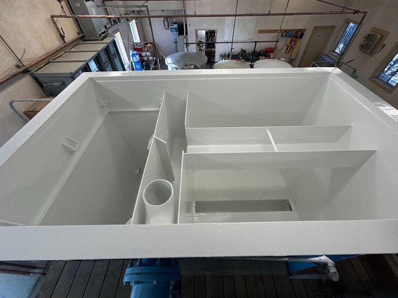 A large white industrial tank with compartments and a pipe, situated in a utility room.