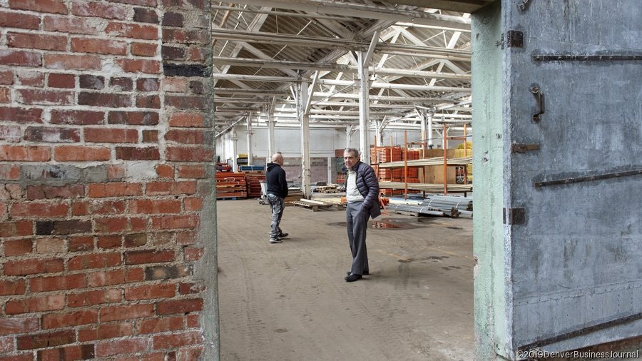 An industrial space with brick walls and metal structures; two men are inspecting the area.