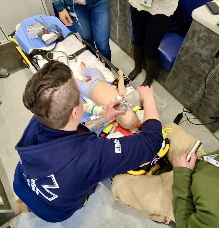Medical personnel train on a child manikin, providing CPR and ventilation on a stretcher.