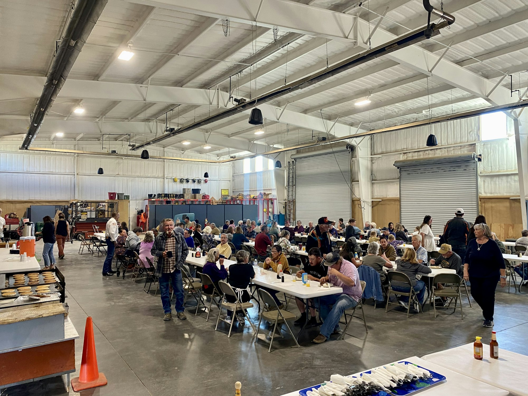People gathered in a large hall, seated at tables, socializing and eating.