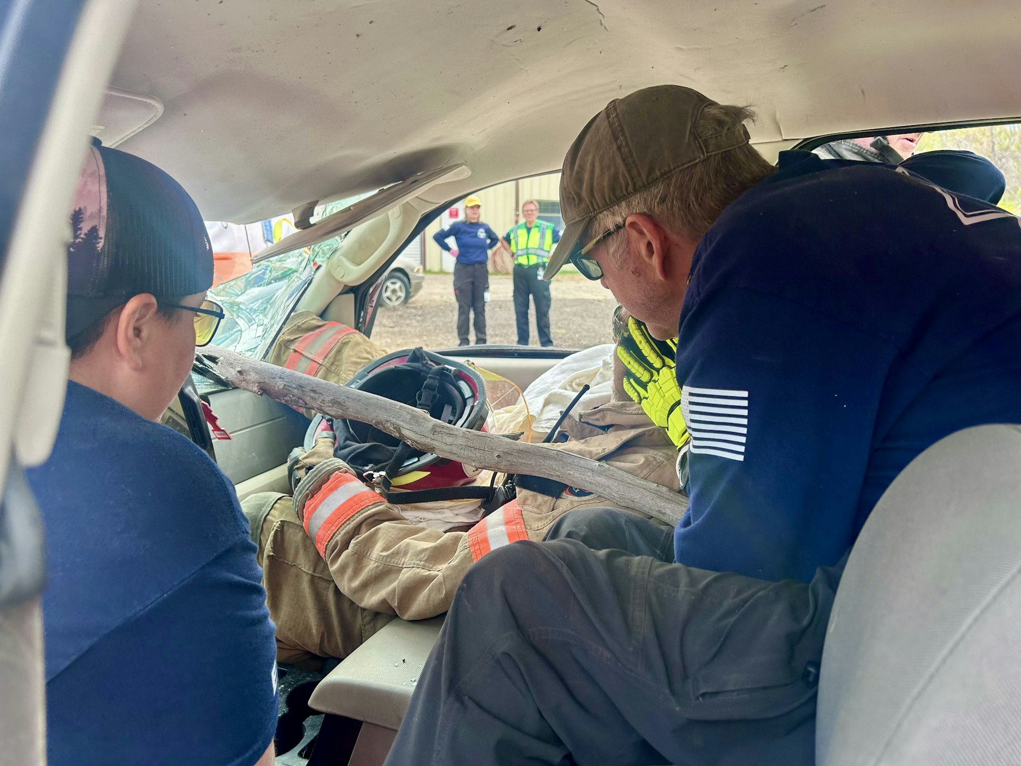 Rescue team assists a person trapped in a car with a stick through the windshield.