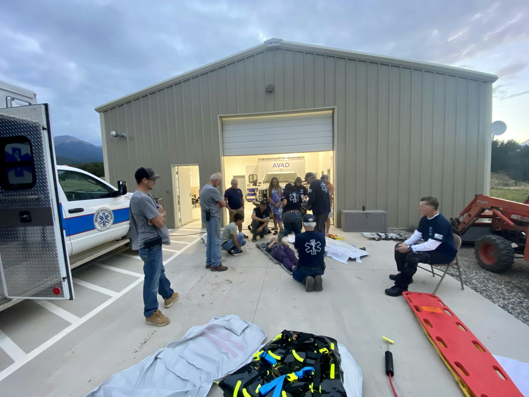 Emergency responders training outside a building with an ambulance and equipment.