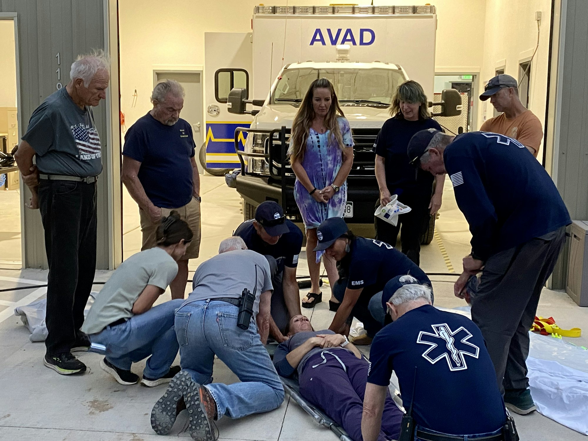 A person on a stretcher surrounded by EMS personnel and onlookers near an ambulance.