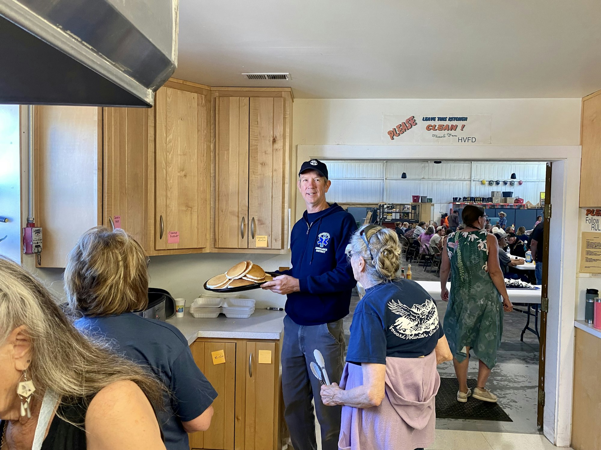 People serving and enjoying food, likely at a community event or gathering; a person holding plates of pancakes.