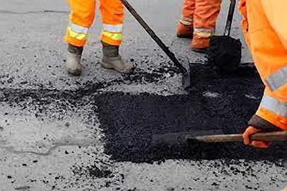 Workers in orange gear fixing asphalt on a road.