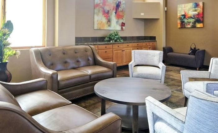 A lounge with leather sofas, armchairs, a round table, abstract art on the walls, and a sideboard with a plant.