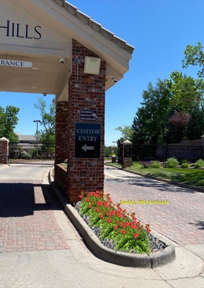 Visitor entry sign on a brick pillar, surrounded by flowers, near a gated area.