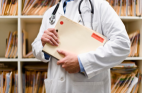 A healthcare professional in a lab coat holds a file in front of a background of medical folders.